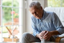 Senior man with knee pain (possibly from arthritis) and holding his knee.